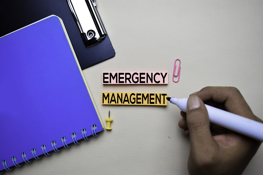 A notebook beside a computer and a person holding a marker with  the words emergency managment.