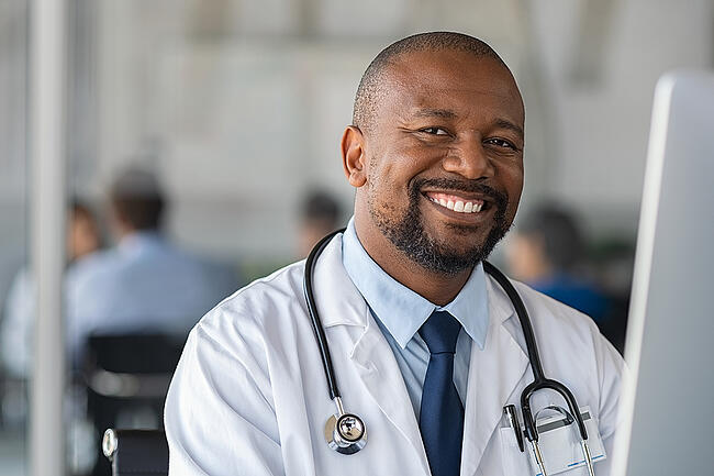 Smiling male nurse manager creating a unit staff schedule on a computer.