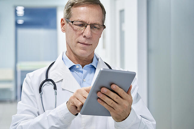 Senior healthcare worker checking staff schedules on a tablet.