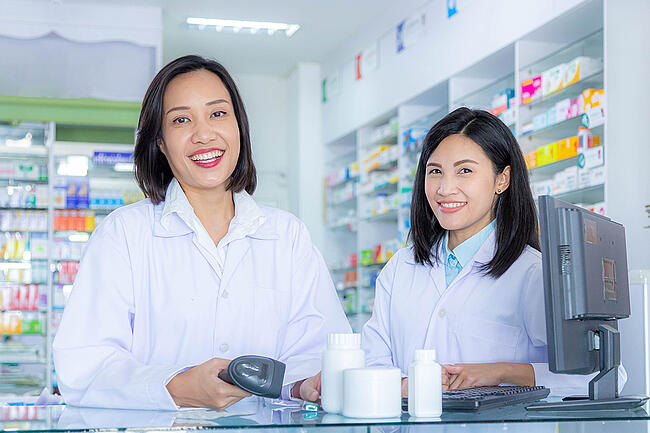 Two pharmacy workers standing behind a desk smiling.