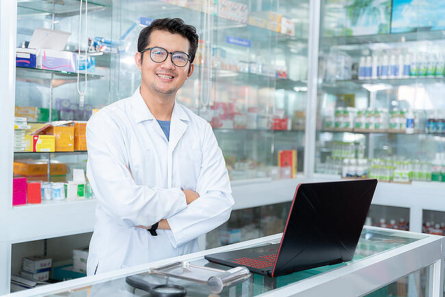 Smiling young pharmacy worker standing behind the pharmacy counter.