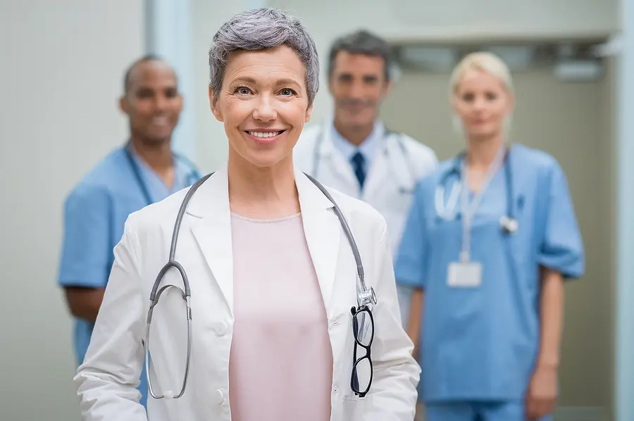 Smiling senior nurse with staff of medical professionals behind her.