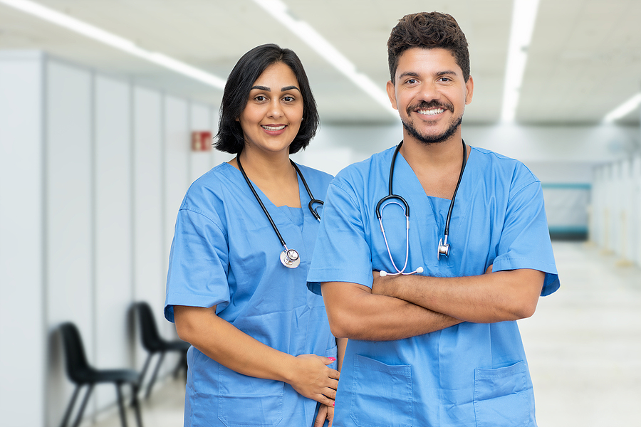 Nurses smiling and looking at the camera. They are standing in the hallway of a hospital.